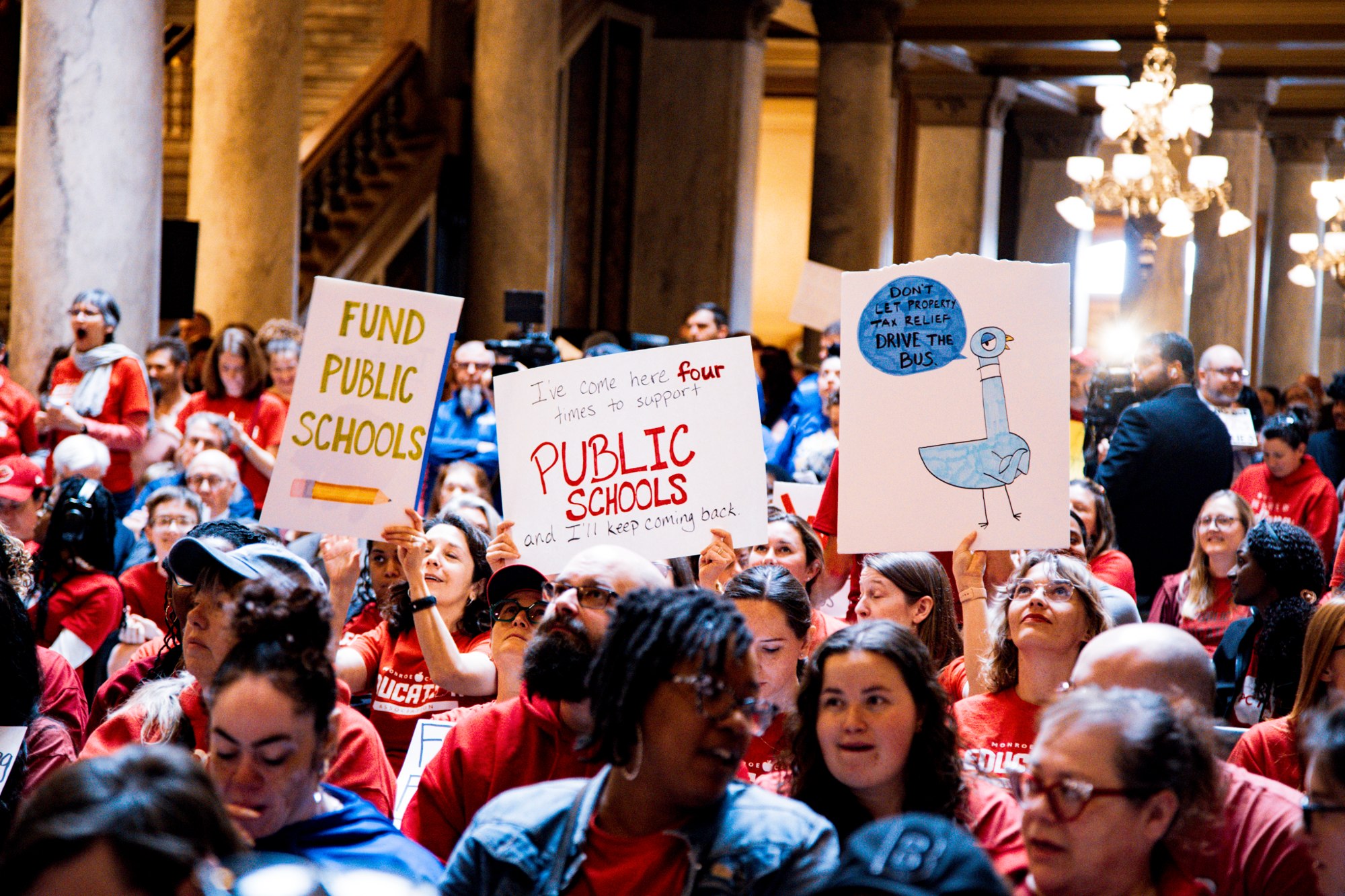 Educators raise public school signs inside the Statehouse